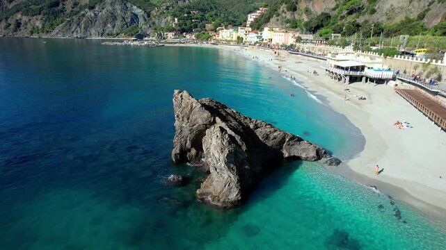 Monterosso al Mare Cinque Terre Italy 4k drone of Fegina beach rock. Cinematic aerial orbital circle flight around Scoglio di Fegina landmark sea stack waterfront resort b-roll landscape