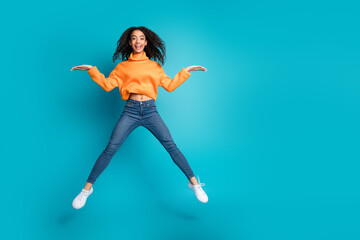 Full length photo of cheerful pretty teen lady dressed orange turtleneck jumping high comparing...