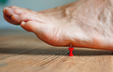 A person's barefoot stepping on a red pushpin tack