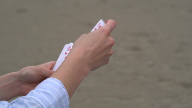 Close-up of a young woman playing cards chooses how to move, looks at the trump card, and puts the card on the deck on the beach. Concept of board card games, getting fun, entertainment