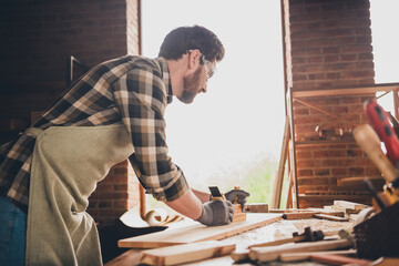 Photo of woodworker guy smooth wood plank with equipment in garage indoors