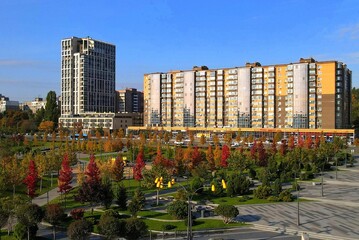 Obraz premium Beautiful autumn park with yellow orange trees and red leaves, buildings, houses, apartment buildings, luxury real estate. Autumn streets in city Dnipro, Ukraine