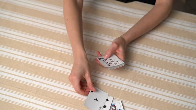 Hands of a young woman dealing classic cards from a deck for playing solitaire at a table. The concept of board card games, having fun, entertainment, poker.