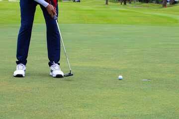 a white golf ball on a tee and a green field ready to be hit with a wood golf stick as a start to a game of golf.