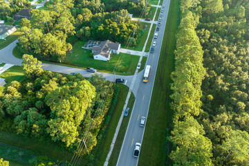 Aerial view of american yellow school bus picking up children at sidewalk bus stop for their...