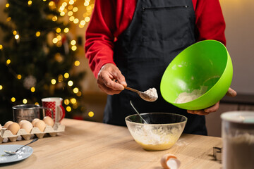 Close-up of man making dough for christmas gingerbread cookies while cooking in cozy decorated kitchen