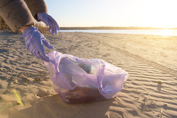 Close-up of hands in gloves collecting plastic waste from the beach. Environmental cleanup and sustainability concept. Perfect for topics on ocean pollution and eco-friendly lifestyle