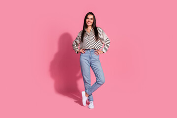 Confident young woman in casual striped shirt and jeans on pink background promoting fashion style