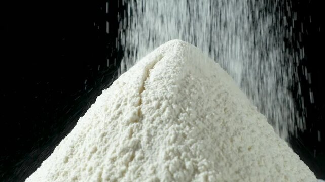 Wheat flour pouring on black background macro slow motion.