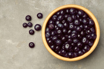 Ripe acai berries in bowl on grey textured table, top view. Space for text