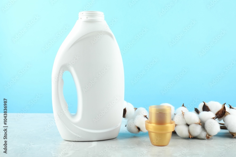 Poster Laundry detergent in bottle, cap and cotton flowers on grey marble table against light blue background