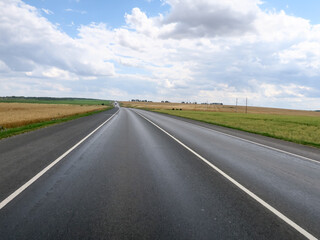New asphalt road surface on the background of green and yellow fields to the horizon. The construction site for the road works. Highway on the background of a rural landscape