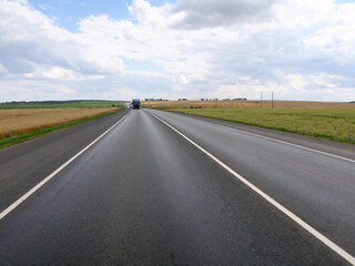 New asphalt road surface on the background of green and yellow fields to the horizon. The construction site for the road works. Highway on the background of a rural landscape