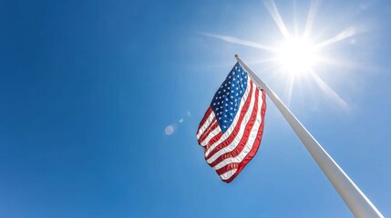 Fototapeta premium The image features an American flag waving against a bright, sunny sky with a notable lens flare, symbolizing patriotism and national pride in a clear, open setting.