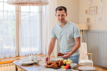 A young cheerful man takes pies from the table on the go