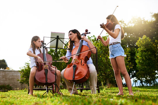 Music, learning and children with violin and cello in park for playing, practice and lesson with teacher. Morning, nature and woman and kids with instruments for talent show, rehearsal or recital