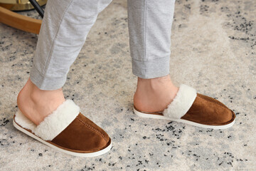 Naklejka premium Comfortable brown suede slippers with white fur lining on a textured carpet floor, cozy home footwear, the cozy footwear provides warmth and relaxation for indoor home activities