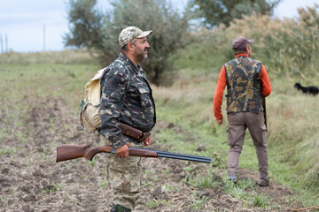 Mature hunter man holding a shotgun and walking through a field