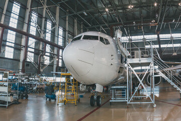 White passenger airliner in the aircraft hangar. Airplane under maintenance. Checking mechanical...