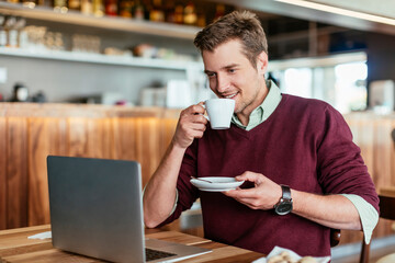 Young man enjoying a coffee in a coffee shop while using a laptop