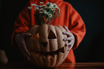 Teenager girl holding carved Halloween pumpkin with flowers inside, close up