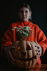 Teenager girl holding carved Halloween pumpkin with flowers inside, close up