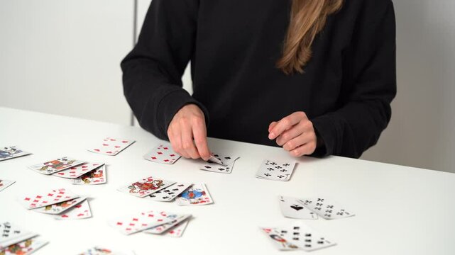 Hands of a young woman choosing and stacking cards while playing solitaire at the table. Entertainment concept, having fun, card board games, poker
