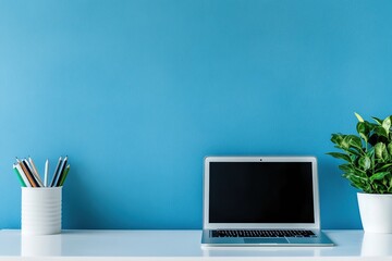 Minimalist workspace with a laptop, plant, and pencils on a white desk against a blue wall.