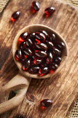 Red krill oil pills or globules on a wooden spoon on a table, close up