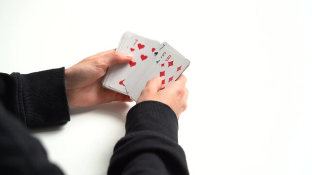 The hands of a young woman hold a deck of cards and look at it and sort it at the table. The concept of board card games, having fun, entertainment, poker, solitaire