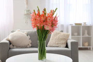 Vase with gladiolus flowers on table in light living room, closeup