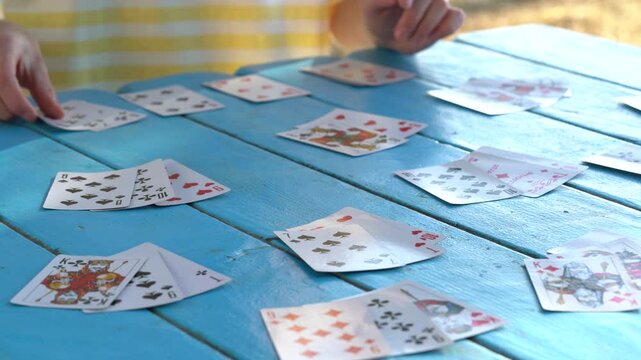 Hands of a young woman choosing and stacking cards while playing solitaire at a blue table. Entertainment concept, having fun, card board games, poker