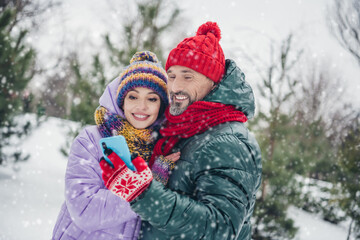 Fototapeta premium Portrait of two positive soulmates embrace hold use telephone spend free time snowy forest outdoors