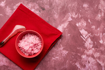 Bowl of natural body scrub, spatula and napkin on color grunge background
