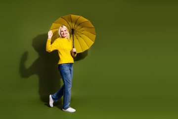 Photo of lovely cheerful lady wear stylish yellow clothes hold parasol walk empty space isolated on...