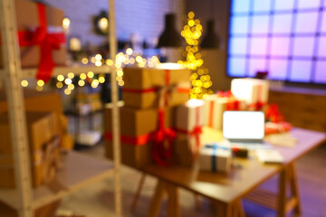 Blurred view of post office with gift boxes, blank laptop and Christmas decorations at evening