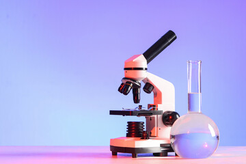 Modern microscope and laboratory flask with liquid on white table