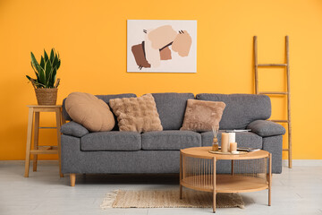 Comfortable sofa, houseplant and burning candles on table near color wall