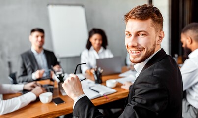 Business Career. Young Businessman At Corporate Meeting With Colleagues Smiling To Camera Sitting In Modern Office.
