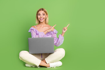 Photo of glad adorable girl sit floor use gadget recommend empty space isolated on green color background