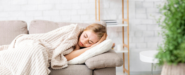 Cold and flu. Afflicted girl laying on couch wrapped in blanket, feeling sick, panorama with copy space