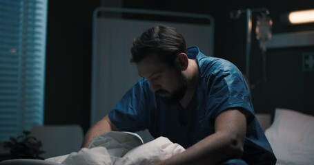 Man in hospital bed, then moves to couch, covers with blanket he's not feeling good.