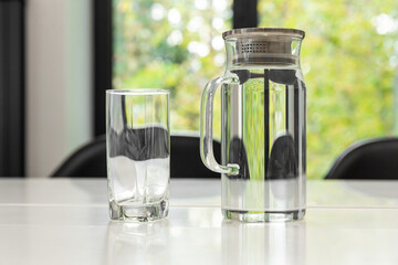 Transparent decanter with water and an empty glass standing on a table.