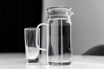 Transparent decanter with water and an empty glass standing on a table.