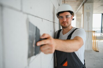 Worker in uniform plastering wall with putty knife indoors