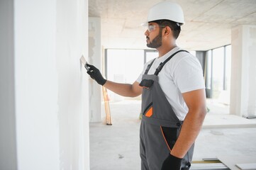 Professional indian worker plastering wall with putty knife indoors.