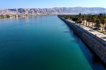 Obraz premium The Nile River flowing through Luxor, with ancient temples and palm trees lining the banks of this life-giving river