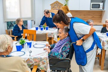 Nurse and elder woman in wheelchair talking at dinning hall