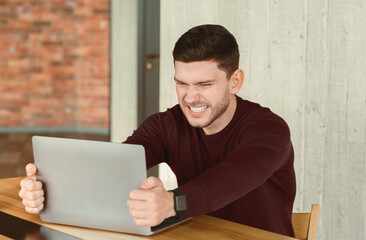 Stressful Job. Mad Office Guy Breaking Laptop Computer Sitting At Workplace Indoor. Selective Focus