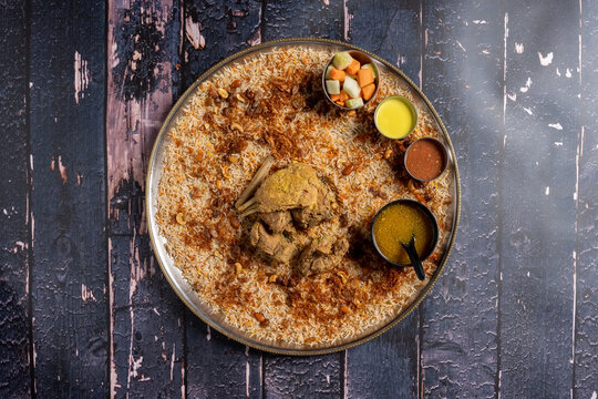 Flat lay of chicken mandi dish with broth, vegetables and sauces